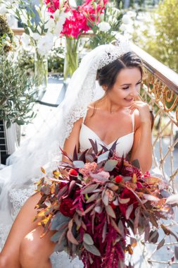 Zarif iç çamaşırlı güzel bir kadın çok katlı bir binanın balkonunda duruyor ve elinde büyük bir buket güzel çiçek tutuyor. Gelinin düğün gününün sabahı.