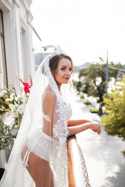 高層ビルのバルコニーには美しいランジェリー姿の若い女性が立っています 結婚式の日の花嫁の朝 — ストック写真
