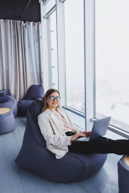 Gündelik kıyafetlerde başarılı kadın, modern bir çalışma alanında masa başında otururken yeni bir proje üzerinde çalışırken bir netbook 'ta daktilo yazmaktır. Ceketli ve gözlüklü bir iş kadını. Telework