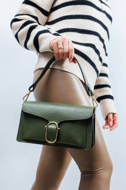 Beyaz arka planda kadın eli olan küçük, yeşil deri bir çanta. Omuz çantası. Yeşil çantalı bir kadın. Tarz, moda, eski moda ve zarafet.
