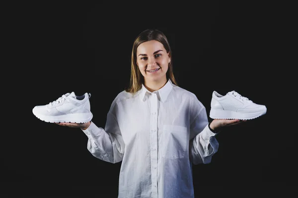 Ljushårig Kvinna Vit Skjorta Svart Bakgrund Håller Vita Sneakers Äkta — Stockfoto