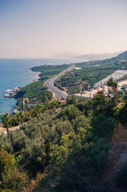 Boş bir asfalt yol güneşli bir yaz gününde nefes kesici kıyı şeridi boyunca esiyor. Berrak mavi gökyüzüne ve sakin Akdeniz 'e bakan kıyı yolunun muhteşem bir görüntüsü..