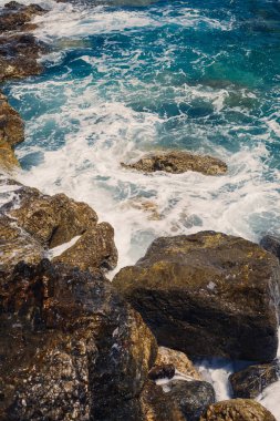 Mavi Akdeniz 'in harika manzarası. Güneşli kayalar, köpüklü dalgalar ve su sıçraması. Dalga kıyıdaki kayalara çarpar.