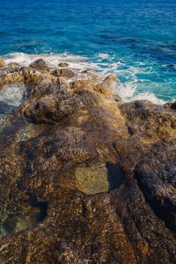 Mavi Akdeniz 'in harika manzarası. Güneşli kayalar, köpüklü dalgalar ve su sıçraması. Dalga kıyıdaki kayalara çarpar.