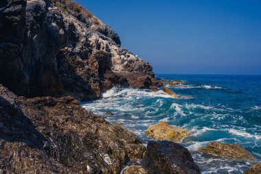 Mavi Akdeniz 'in harika manzarası. Güneşli kayalar, köpüklü dalgalar ve su sıçraması. Dalga kıyıdaki kayalara çarpar.