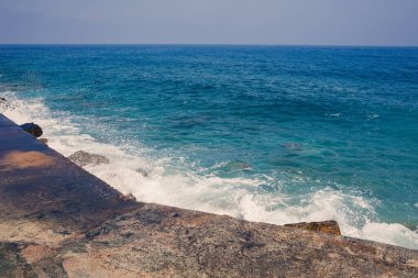 Deniz suyu kayalık kayalara çarpar ve köpükle dalgalar yaratır.