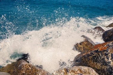 Deniz suyu kayalık kayalara çarpar ve köpükle dalgalar yaratır.