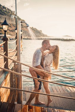 Deniz kenarında mutlu bir çift. Bir adam ve bir kız açık hava rıhtımında duşun altındalar. Tatildeki mutlu çift. Deniz kenarındaki kadın ve erkek.