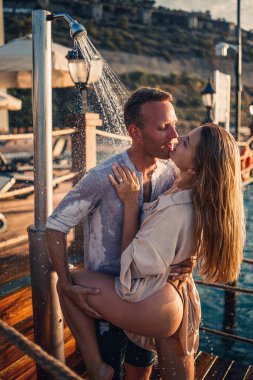 Deniz kenarında mutlu bir çift. Bir adam ve bir kız açık hava rıhtımında duşun altındalar. Tatildeki mutlu çift. Deniz kenarındaki kadın ve erkek.