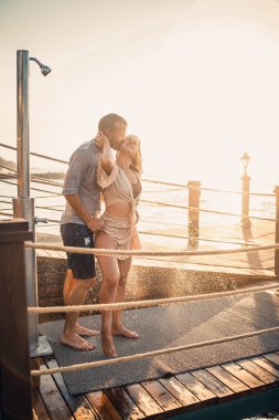 Deniz kenarında mutlu bir çift. Bir adam ve bir kız açık hava rıhtımında duşun altındalar. Tatildeki mutlu çift. Deniz kenarındaki kadın ve erkek.