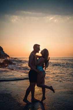 Deniz kenarında gün batımının arka planında birbirine aşık güzel bir çift. Genç bir kadın ve erkek gün batımında deniz kenarında sarılıyor.