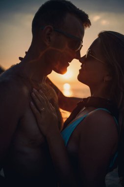 Deniz kenarında gün batımının arka planında birbirine aşık güzel bir çift. Genç bir kadın ve erkek gün batımında deniz kenarında sarılıyor.