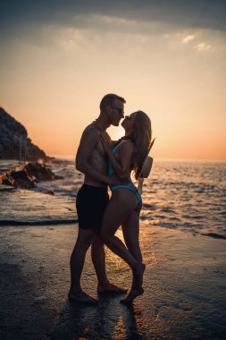 Deniz kenarında gün batımının arka planında birbirine aşık güzel bir çift. Genç bir kadın ve erkek gün batımında deniz kenarında sarılıyor.