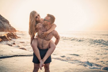 Sevgi dolu bir çift deniz kenarında yürüyor. Akdeniz kıyısında gün batımında genç bir aile. Tatil konsepti. Gün batımında mayolu bir kadın ve deniz kenarında şortlu bir adam. Seçici odak.