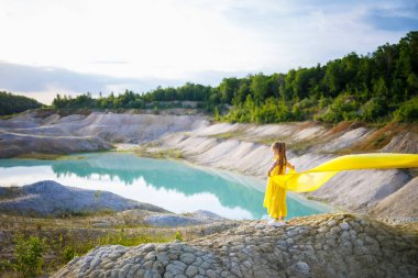 Göl kenarında sarı kumaşlı sarı kanatlı sarı elbiseli 6-7 yaşlarında Ukraynalı bir kız. Mavi gökyüzü ve sarı kumaş, Ukrayna bayrağının renkleri..