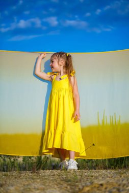 Ukraynalı 7 yaşında, Ukraynalı bir vatansever, mavi gökyüzüne karşı sarı bir elbise giymiş. Mavi gökyüzü. Güneşli bir gün. Özgür Ukraynalı çocuk. Ukrayna 'nın çocuk sembolü