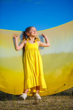 Ukraynalı 7 yaşında, Ukraynalı bir vatansever, mavi gökyüzüne karşı sarı bir elbise giymiş. Mavi gökyüzü. Güneşli bir gün. Özgür Ukraynalı çocuk. Ukrayna 'nın çocuk sembolü