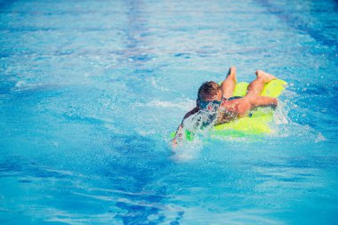 Yakışıklı genç adam mavi havuzda şişme yatakta yüzüyor.