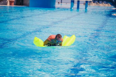 Yakışıklı genç adam mavi havuzda şişme yatakta yüzüyor.