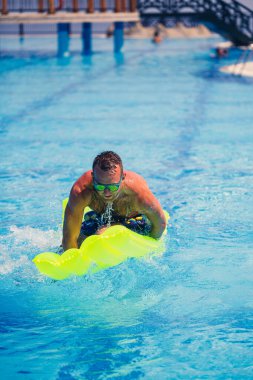 Yakışıklı genç adam mavi havuzda şişme yatakta yüzüyor.