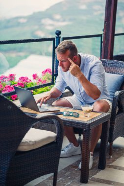 Duygusal bir adam tatilde bilgisayarın başına oturur ve çalışır. Freelancer tatildeyken çalışıyor. Yüksek kalite fotoğraf