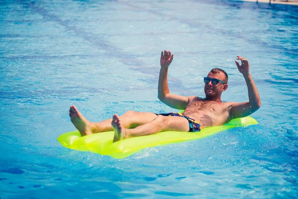 一个年轻人在一个黄色的充气床垫上沐浴在游泳池里 度假时在阳光下放松 快乐的成功人士 — 图库照片