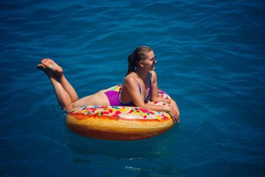 Mavi denizde gevşeyen şişme yüzüklü mayolu güzel, mutlu genç bir kadın. Güneşli bir gün, deniz kenarında tatil, turizm