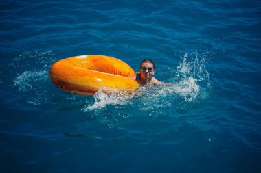 Güzel genç bir kadın şişirilebilir bir çemberden mavi denize düştü. Tatildeki kız denizde daireler çizerek yüzüyor