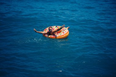 Şeffaf turkuaz denizde şişme bir çöreğin üzerinde yüzen genç bir kadın. İnce bir bayanın Türkiye, Mısır ve Akdeniz 'de tatil yaparken dinlenmesi.