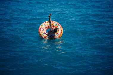 Şeffaf turkuaz denizde şişme bir çöreğin üzerinde yüzen genç bir kadın. İnce bir bayanın Türkiye, Mısır ve Akdeniz 'de tatil yaparken dinlenmesi.