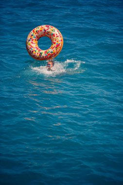 Şeffaf turkuaz denizde şişme bir çöreğin üzerinde yüzen genç bir kadın. İnce bir bayanın Türkiye, Mısır ve Akdeniz 'de tatil yaparken dinlenmesi.