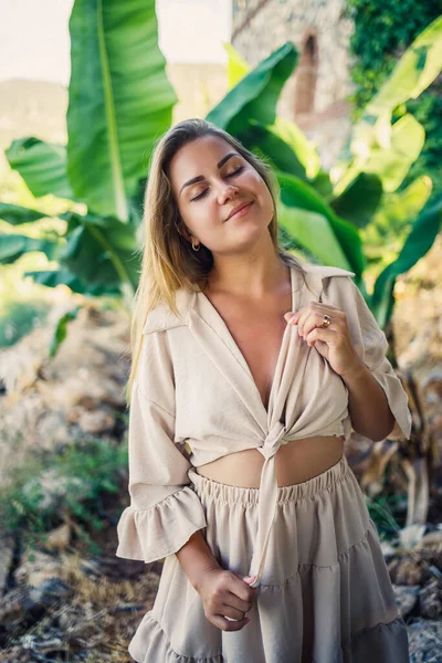 Çekici, genç, açık tenli kadın tropikal parkta muz ağaçlarının yanında duruyor..