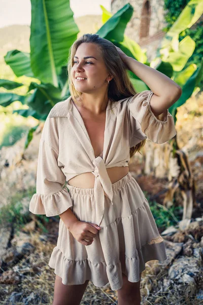 Çekici, genç, açık tenli kadın tropikal parkta muz ağaçlarının yanında duruyor..