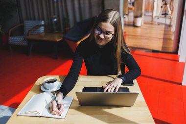 İnternette bir kafede çalışıyorum. Günlük kıyafetleri ve gözlükleriyle dizüstü bilgisayar kullanan mutlu bir kız. Şehirde rahat bir yaşam tarzı için modern dijital teknolojilerle uzaktan çalışma veya eğitim.