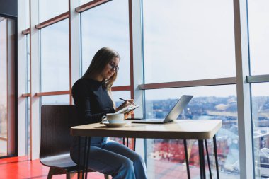 İnternette bir kafede çalışıyorum. Günlük kıyafetleri ve gözlükleriyle dizüstü bilgisayar kullanan mutlu bir kız. Şehirde rahat bir yaşam tarzı için modern dijital teknolojilerle uzaktan çalışma veya eğitim.