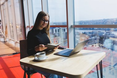 İnternette bir kafede çalışıyorum. Günlük kıyafetleri ve gözlükleriyle dizüstü bilgisayar kullanan mutlu bir kız. Şehirde rahat bir yaşam tarzı için modern dijital teknolojilerle uzaktan çalışma veya eğitim.