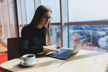 İnternette bir kafede çalışıyorum. Günlük kıyafetleri ve gözlükleriyle dizüstü bilgisayar kullanan mutlu bir kız. Şehirde rahat bir yaşam tarzı için modern dijital teknolojilerle uzaktan çalışma veya eğitim.