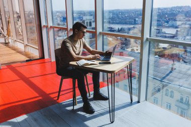 Genç milenyum erkeği çevrimiçi çalışırken dizüstü bilgisayarın önünde oturuyor. Modern dijital göçebe çalışmaları, kafenin iç kısımlarında netbook 'ta serbest çalışma üzerine