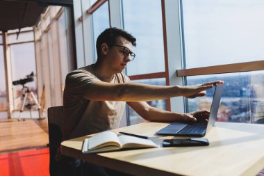 Gözlüklü, gülümseyen, zeki, genç bir serbest yazar bir kafede vakit geçirirken dizüstü bilgisayarda çalışıyor. Pozitif bir öğrenci bir kafede ahşap bir masada oturur. Mutlu adam içeride çalışırken oturuyor.