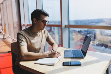 Gözlüklü, gülümseyen, zeki, genç bir serbest yazar bir kafede vakit geçirirken dizüstü bilgisayarda çalışıyor. Pozitif bir öğrenci bir kafede ahşap bir masada oturur. Mutlu adam içeride çalışırken oturuyor.