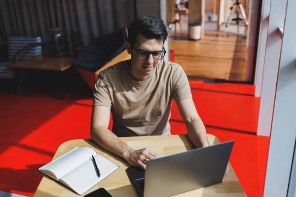 Genç milenyum erkeği çevrimiçi çalışırken dizüstü bilgisayarın önünde oturuyor. Modern dijital göçebe çalışmaları, kafenin iç kısımlarında netbook 'ta serbest çalışma üzerine