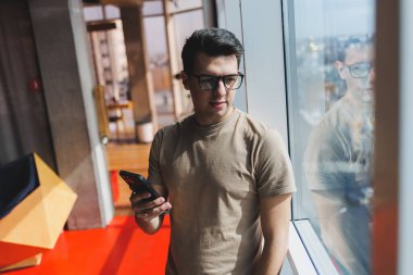 Neşeli Scofe erkek girişimci ofis penceresinin yanında duruyor ve şirkette çalışırken gülümsüyor başarılı şirket patronu zengin yaşam tarzından memnun.