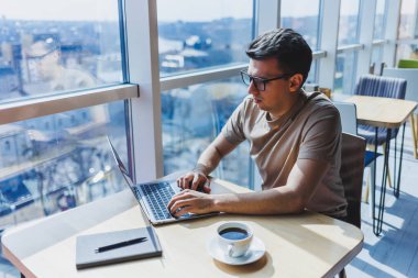 Gözlüklü, gülümseyen, zeki, genç bir serbest yazar bir kafede vakit geçirirken dizüstü bilgisayarda çalışıyor. Pozitif bir öğrenci bir kafede ahşap bir masada oturur. Mutlu adam içeride çalışırken oturuyor.