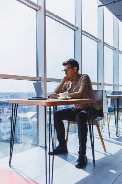 Genç ve çekici bir erkek serbest yazar bir kahve dükkanının içinde oturur ve pencereden dışarı bakar. Yakışıklı blogcu laptopta fikirler yazarken kafedeki tahta masada dizüstü bilgisayarla oturuyor.