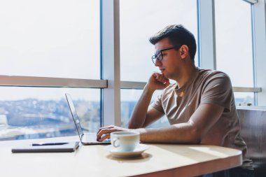 Gözlüklü, gülümseyen, zeki, genç bir serbest yazar bir kafede vakit geçirirken dizüstü bilgisayarda çalışıyor. Pozitif bir öğrenci bir kafede ahşap bir masada oturur. Mutlu adam içeride çalışırken oturuyor.