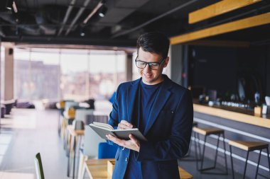 Kafede not defteriyle çalışan serbest çalışan genç bir adam, not defterli bir iş adamı, ceket ve gözlüklü bir adam.