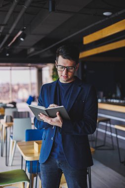 Kafede not defteriyle çalışan serbest çalışan genç bir adam, not defterli bir iş adamı, ceket ve gözlüklü bir adam.