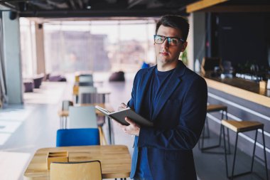 Kafede not defteriyle çalışan serbest çalışan genç bir adam, not defterli bir iş adamı, ceket ve gözlüklü bir adam.