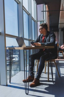 Gözlüklü neşeli serbest çalışan akıllı telefonlu ve gülümseyen gün boyunca kafede dizüstü bilgisayarlı ve not defterli bir masada oturuyor. Ofisten uzakta çalışıyor..