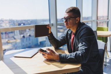Gözlüklü neşeli serbest çalışan akıllı telefonlu ve gülümseyen gün boyunca kafede dizüstü bilgisayarlı ve not defterli bir masada oturuyor. Ofisten uzakta çalışıyor..